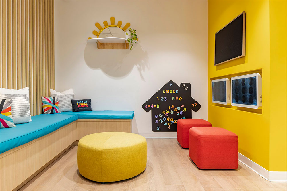 Colorful pediatric dental office design with bench seating, play wall, and bright yellow accents in a kid-friendly waiting area