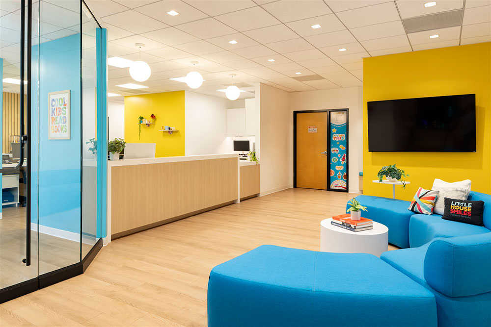 Modern pediatric dental reception with blue seating, yellow accent wall, front desk, and bright, welcoming waiting area