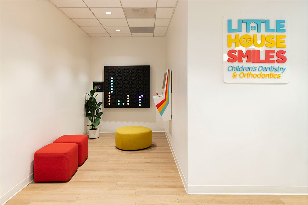 Pediatric dental waiting area with colorful seating, interactive wall game, arcade console, and branded signage