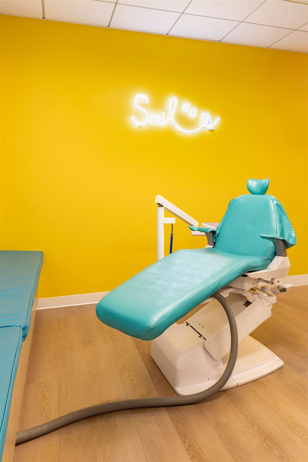 Bright pediatric dental room with teal chair, bold yellow wall, and neon smile sign creating a playful atmosphere