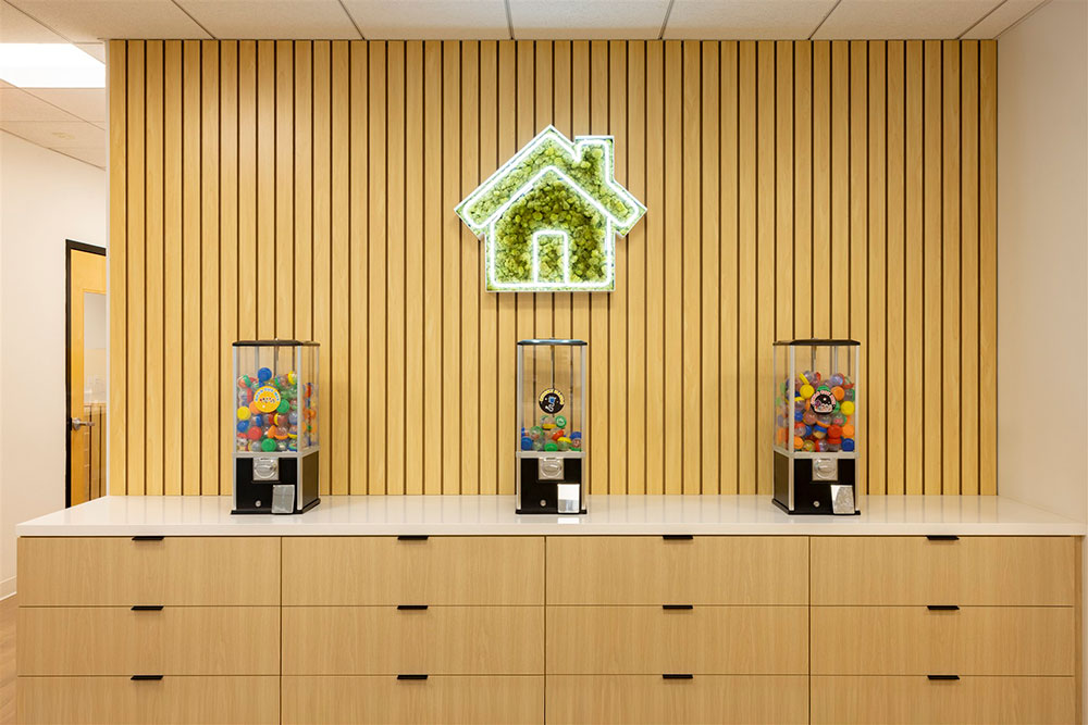 Modern pediatric dental office display with wood slat wall, prize machines, cabinetry, and illuminated logo centerpiece