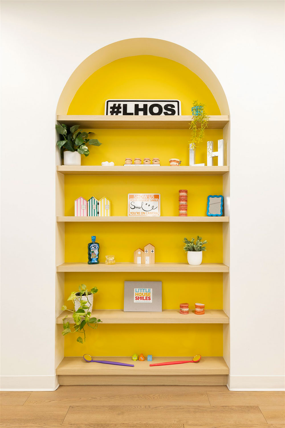 Built-in shelving with yellow accent wall displaying dental decor, plants, and kid-friendly items in pediatric office